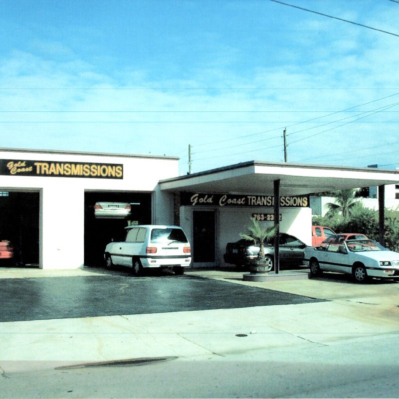 Front view of the Gold Coast Transmissions auto repair shop with service bays and parked vehicles